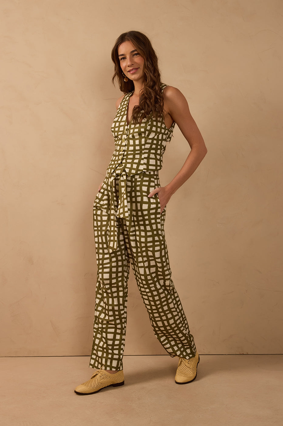 Model wearing olive green and ivory geometric wide-leg pants with a matching fabric tie belt, styled with a coordinating sleeveless vest from TYNA Collection.
