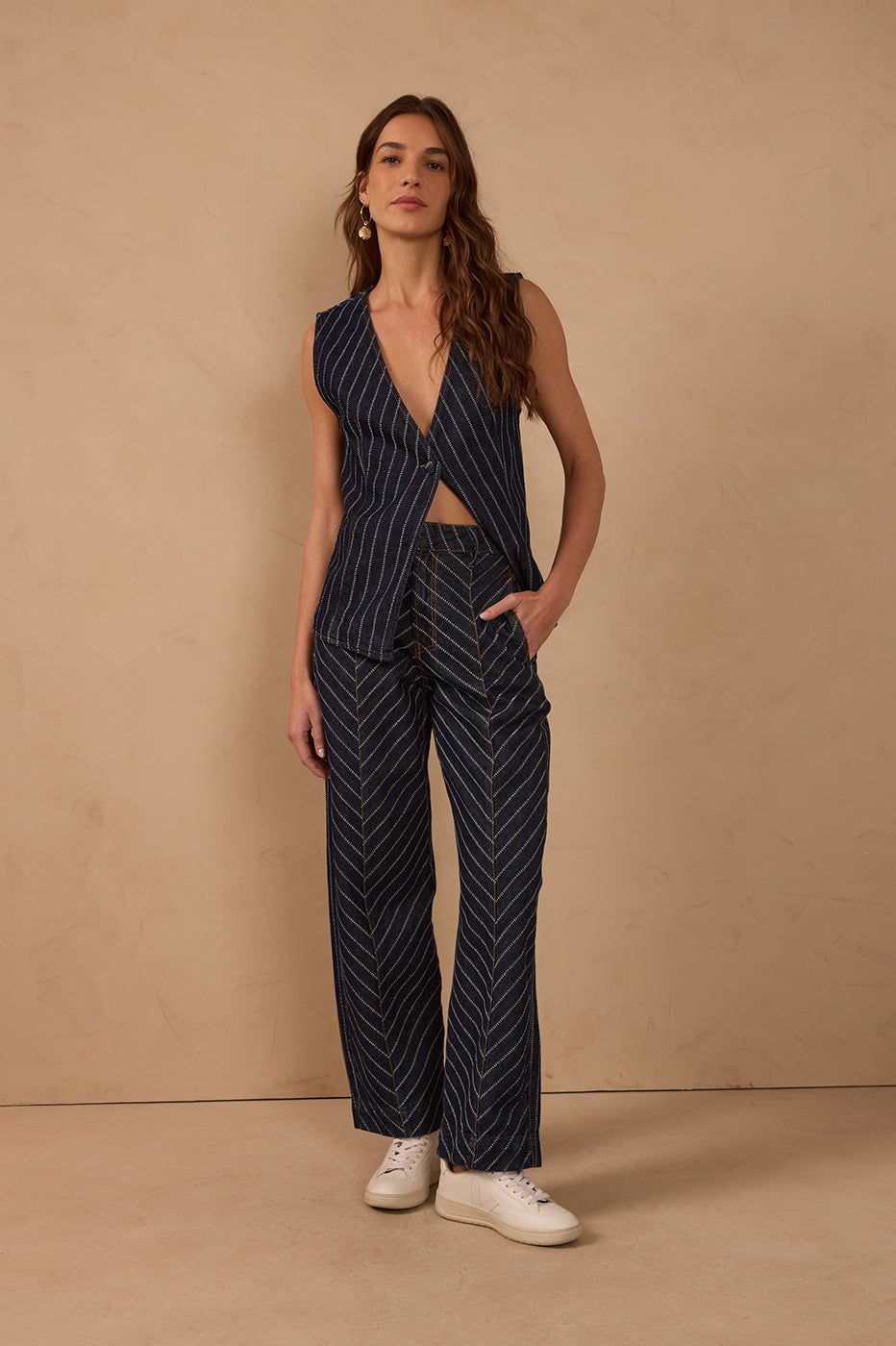 Model wearing dark blue denim striped barrel pants with belt loops and pockets, styled with a matching sleeveless striped vest and white sneakers.