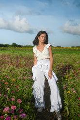 Model wearing white wide leg pants with a high rise waistband and front tie, styled with a white ruffled crop top in a flower field.