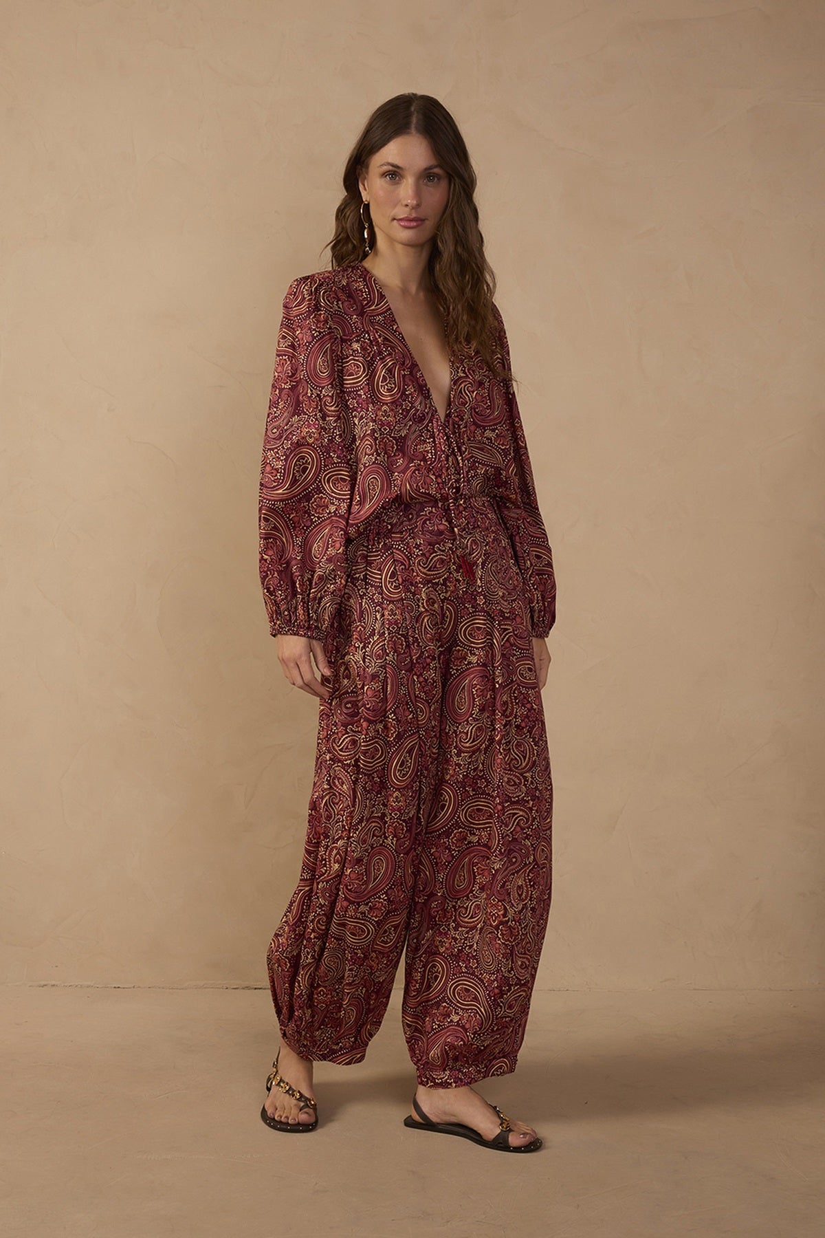 Model wearing Brown Noite paisley barrel pants in burgundy and brown tones with a relaxed tapered silhouette, styled with the matching V-neck paisley blouse and flat sandals.