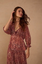 Model wearing the Brown Garoa ruffled mesh blouse featuring a dusty rose and brown animal-inspired print, V-neckline, gathered waist, and ruffled sleeves, styled with a coordinating printed skirt.