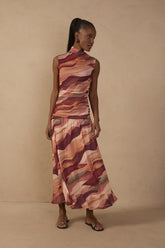 Model wearing the Multicolor Dunas High Neck Mesh Maxi Dress featuring an abstract sunset-inspired print in terracotta, peach, burgundy and olive tones, with a ruched bodice and flowing maxi skirt.