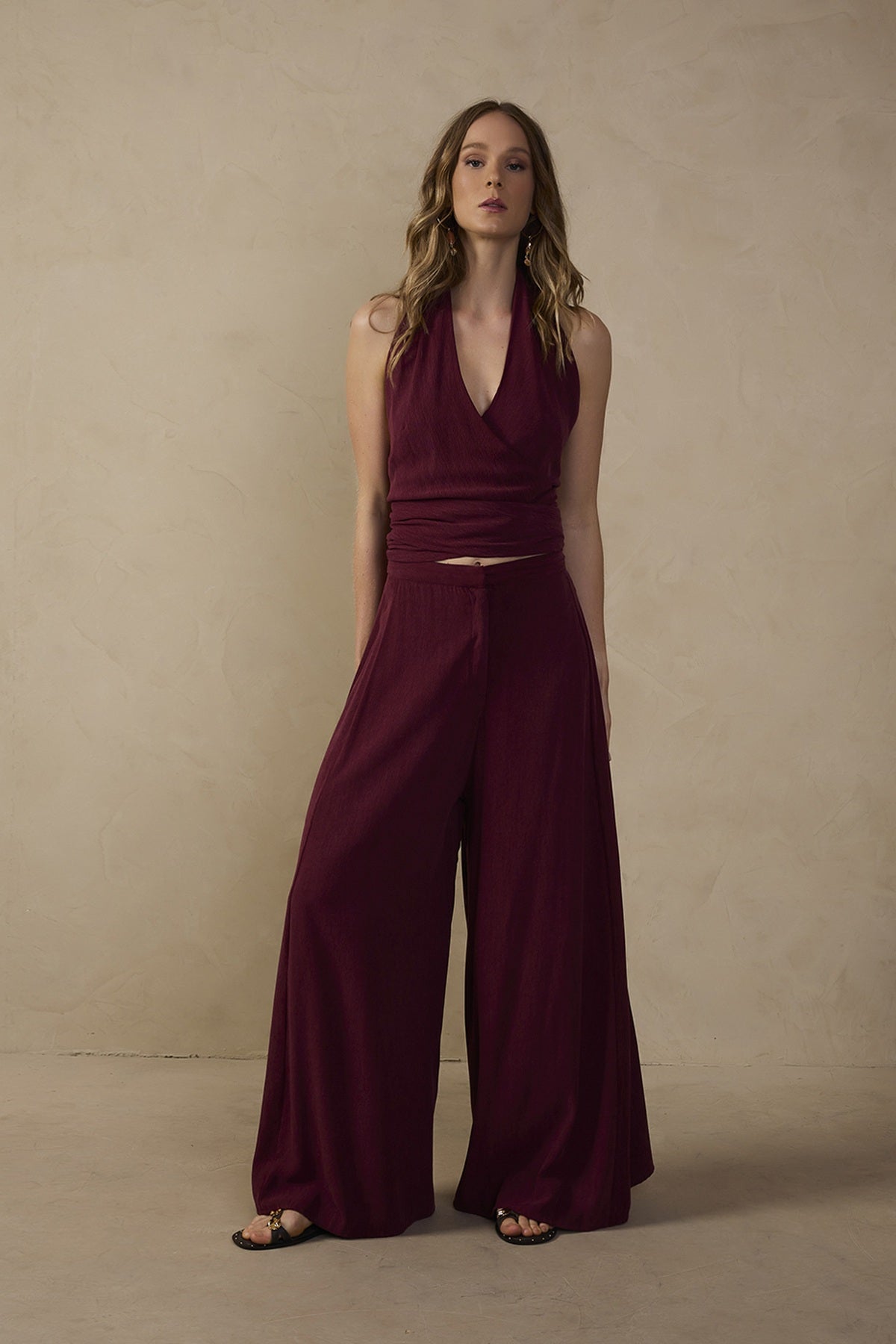 Model wearing Sienna burgundy wide-leg pants featuring a flowing full-length silhouette and clean waistband, styled with a matching burgundy halter top and black sandals.