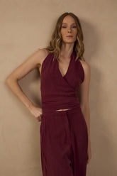 Model wearing the Sienna Burgundy Halter Neck Top featuring a deep V-neckline, sleeveless halter design, and gathered ruched waist, styled with matching burgundy wide-leg pants.