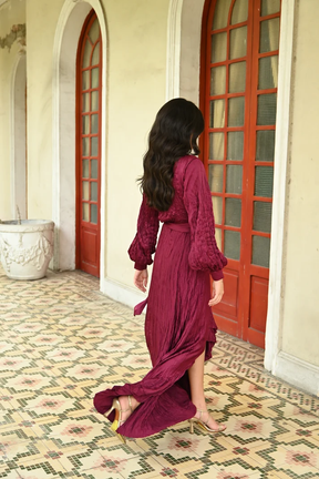 Burgundy textured wrap maxi dress with long balloon sleeves, flowing high-low hem, and tie waist, shown from the back – TYNA Collection.