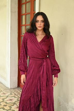Elegant wine burgundy maxi dress featuring a V-neck wrap bodice, crinkled texture, long puff sleeves, and satin waist tie TYNA Collection.