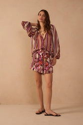 Model wearing Jazmin floral print shorts in burgundy, pink, coral and ivory with a contrasting striped hem, styled with the Aurora Stripes Blouse and flat sandals.