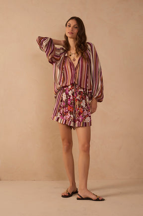 Model wearing Jazmin floral print shorts in burgundy, pink, coral and ivory with a contrasting striped hem, styled with the Aurora Stripes Blouse and flat sandals.